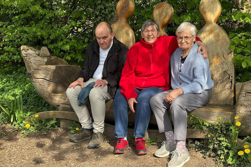 Bild zeigt drei Personen auf einer Bank im Wald.
